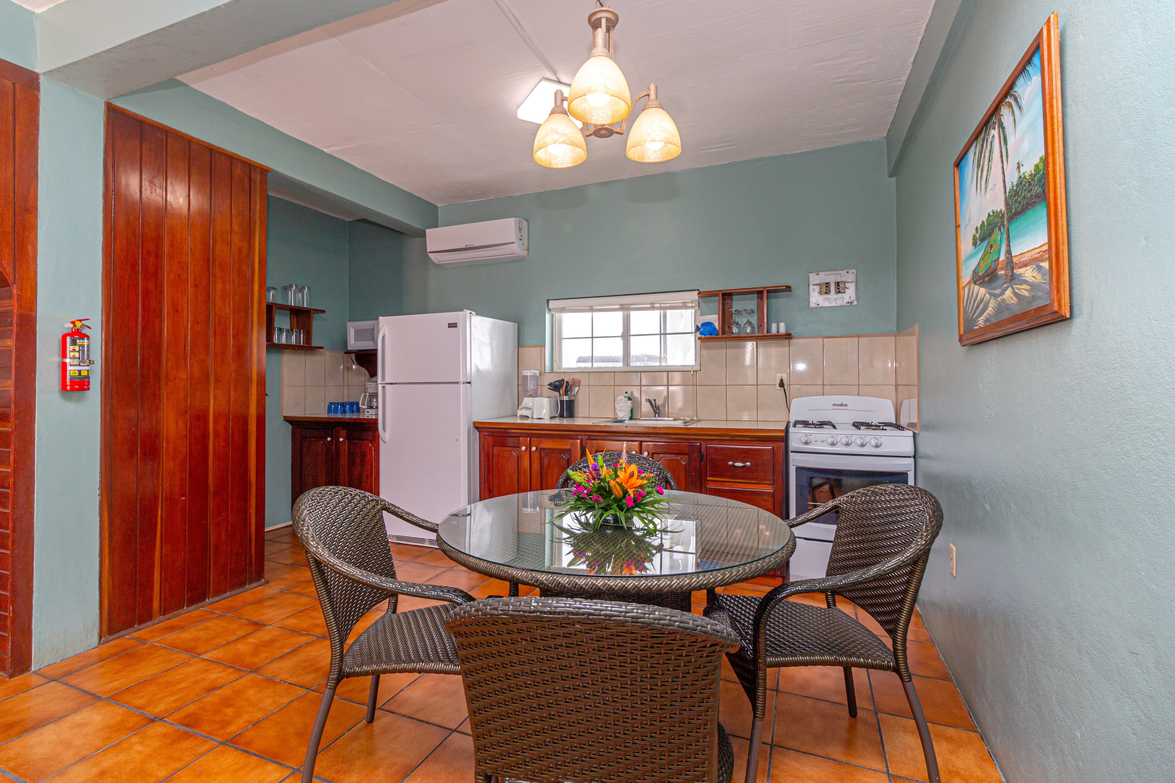 A dining area with a round table and chairs next to a small kitchenette with white appliances and wo