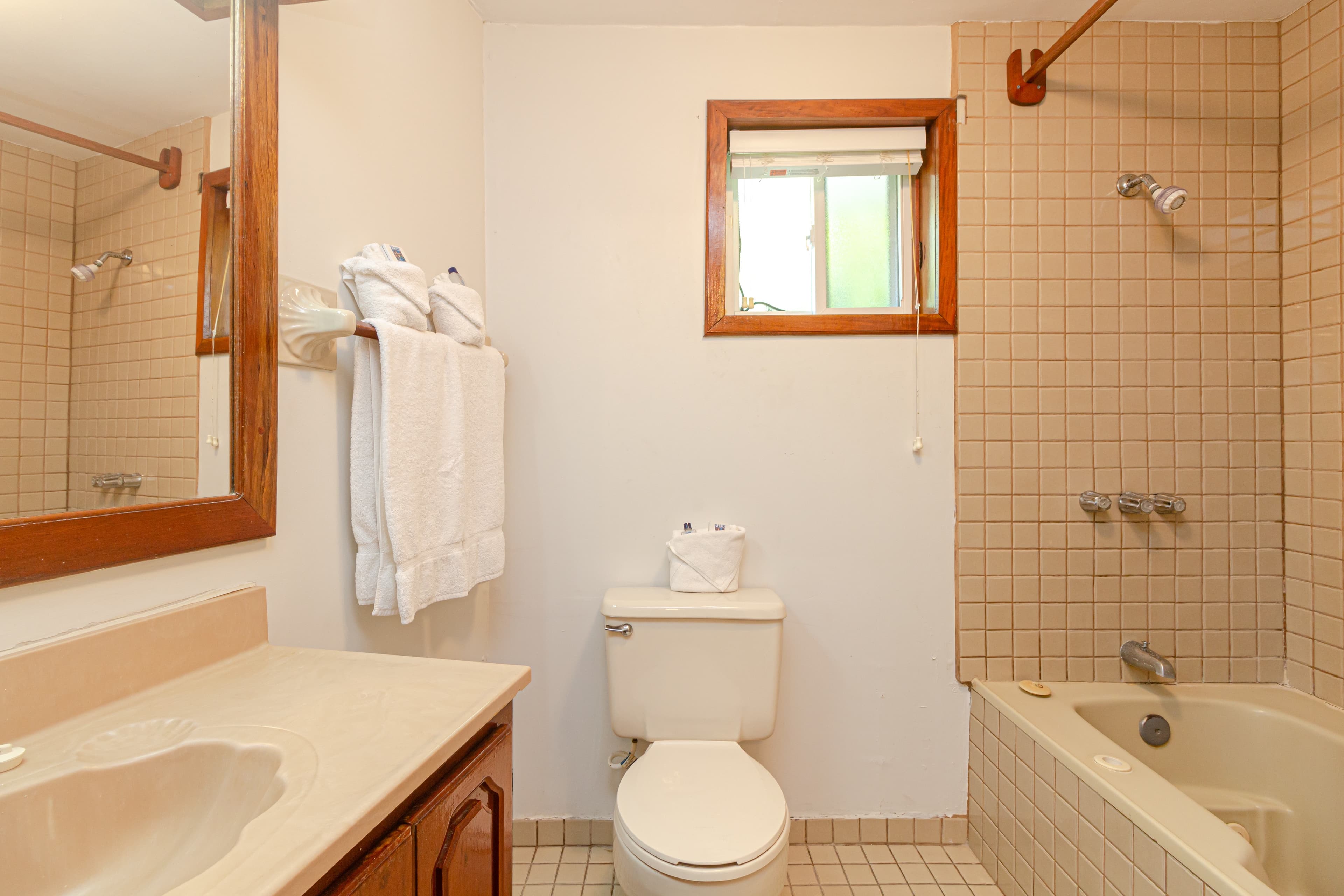 A bathroom with a bathtub and shower, a white toilet, a wooden-framed mirror above a sink, and beige