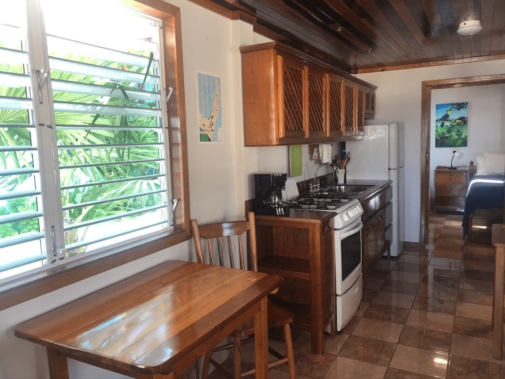 Kitchen table and chairs under window, kitchen cabinets, stove and refrigerator, and doorway leading