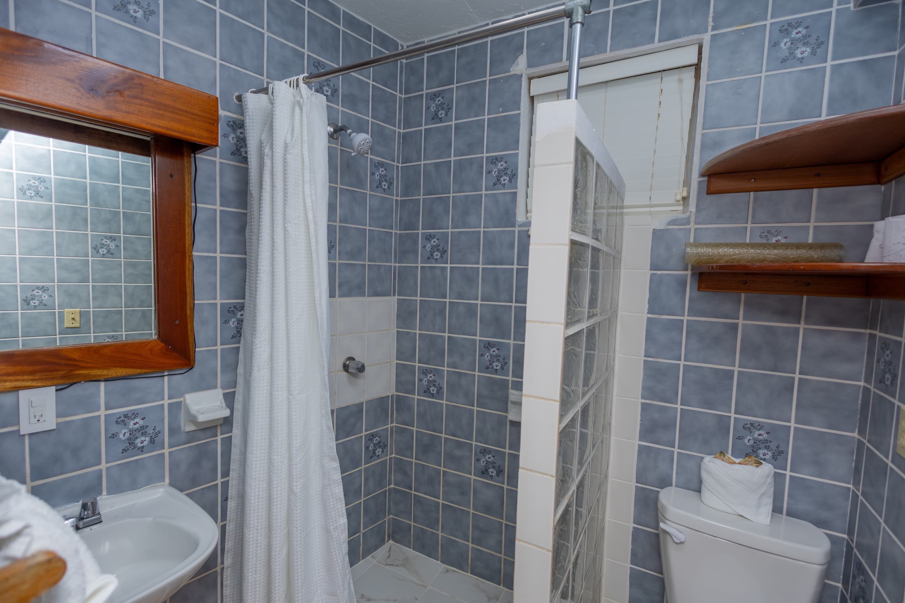 A compact bathroom with blue and gray patterned tiles, a wooden-framed mirror above a white sink, a