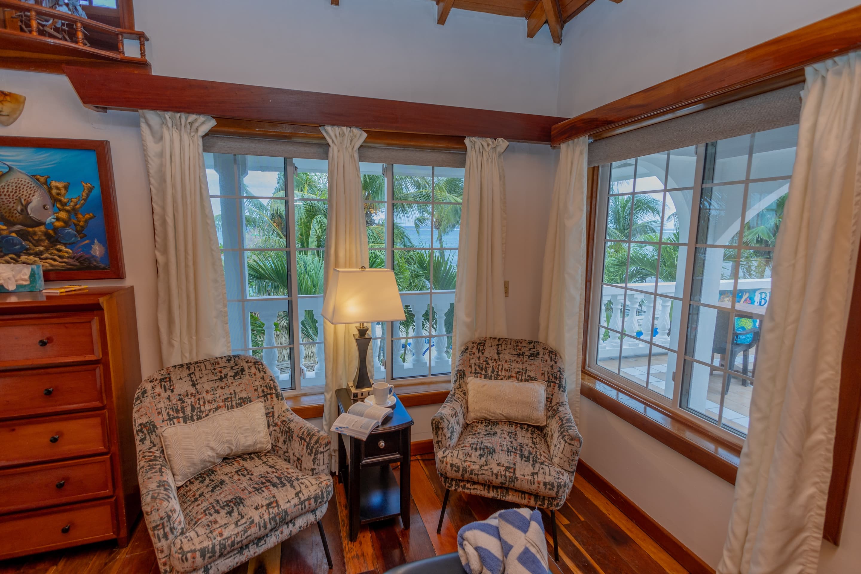 A sitting area with two patterned armchairs, a small table with a lamp, and windows with sheer curta