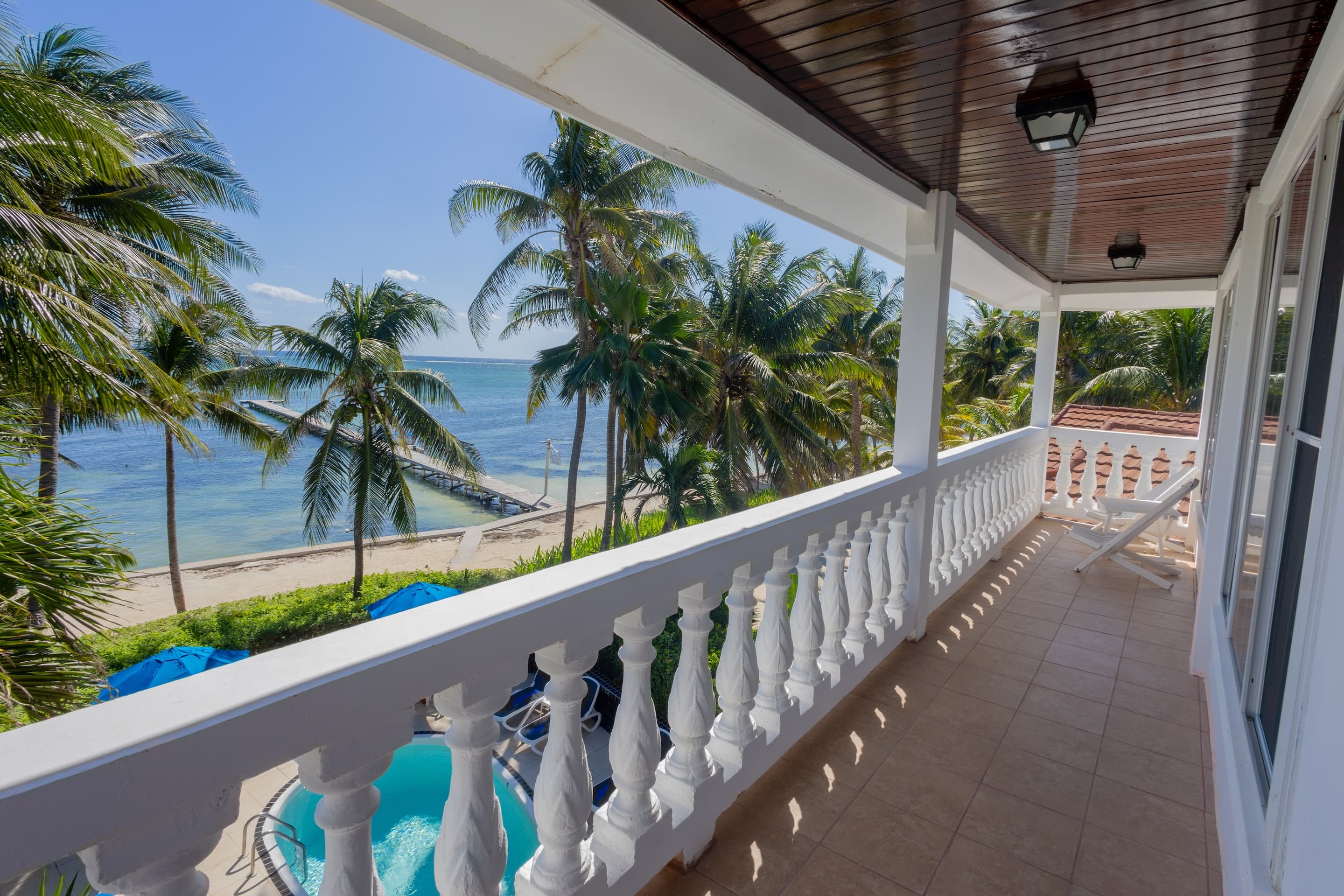 A long, covered balcony with white balustrades and a tiled floor, offering a scenic view of a tropic