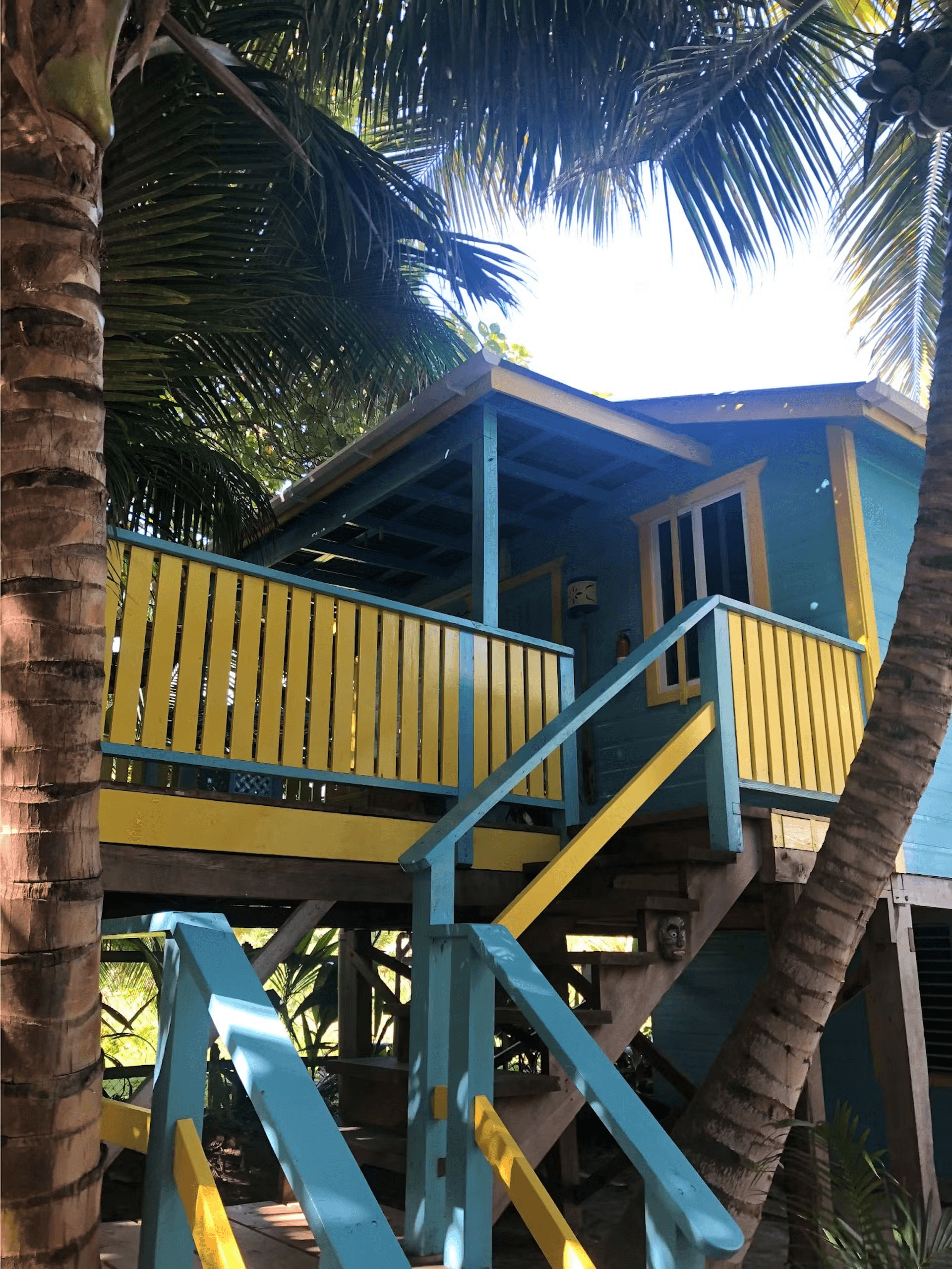Exterior of a colorful blue and yellow painted cabana with stairs leading to second level, surrounde