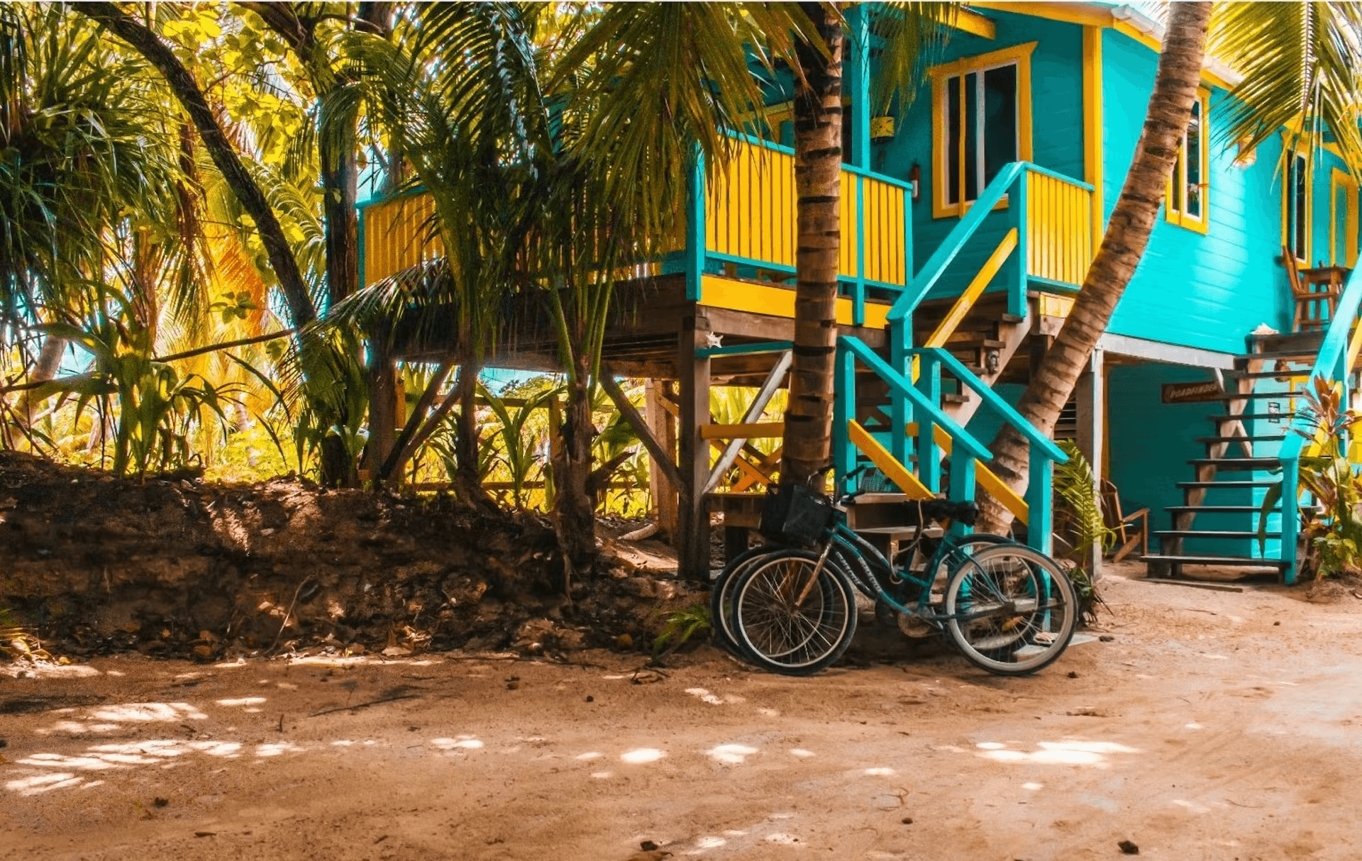 Ground view of a brightly painted blue and white cabana with bicycle leaning against base of stairs