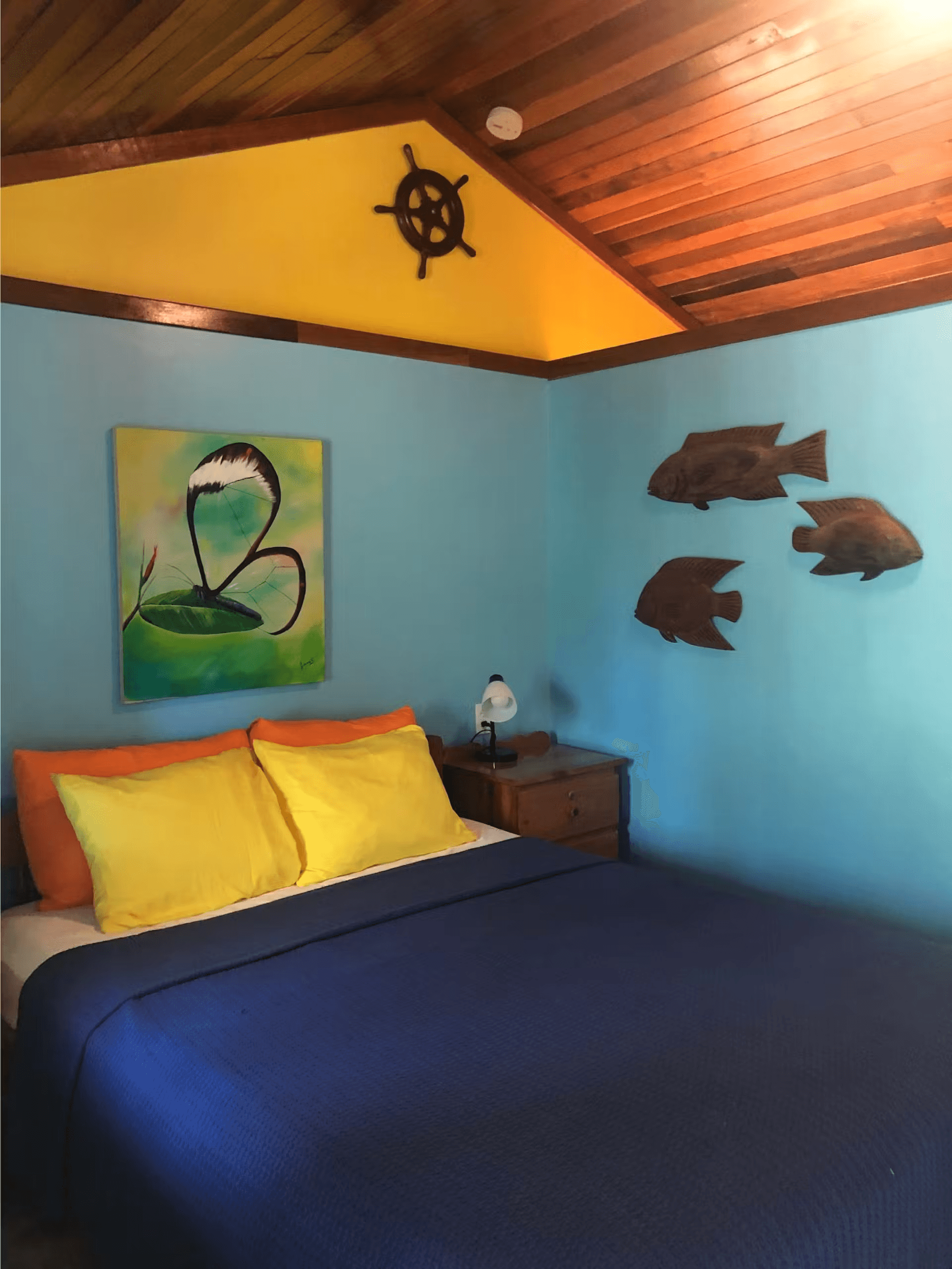 Bedroom decorated in shades of blue and yellow with queen bed, vaulted wood ceilings, three wooden d