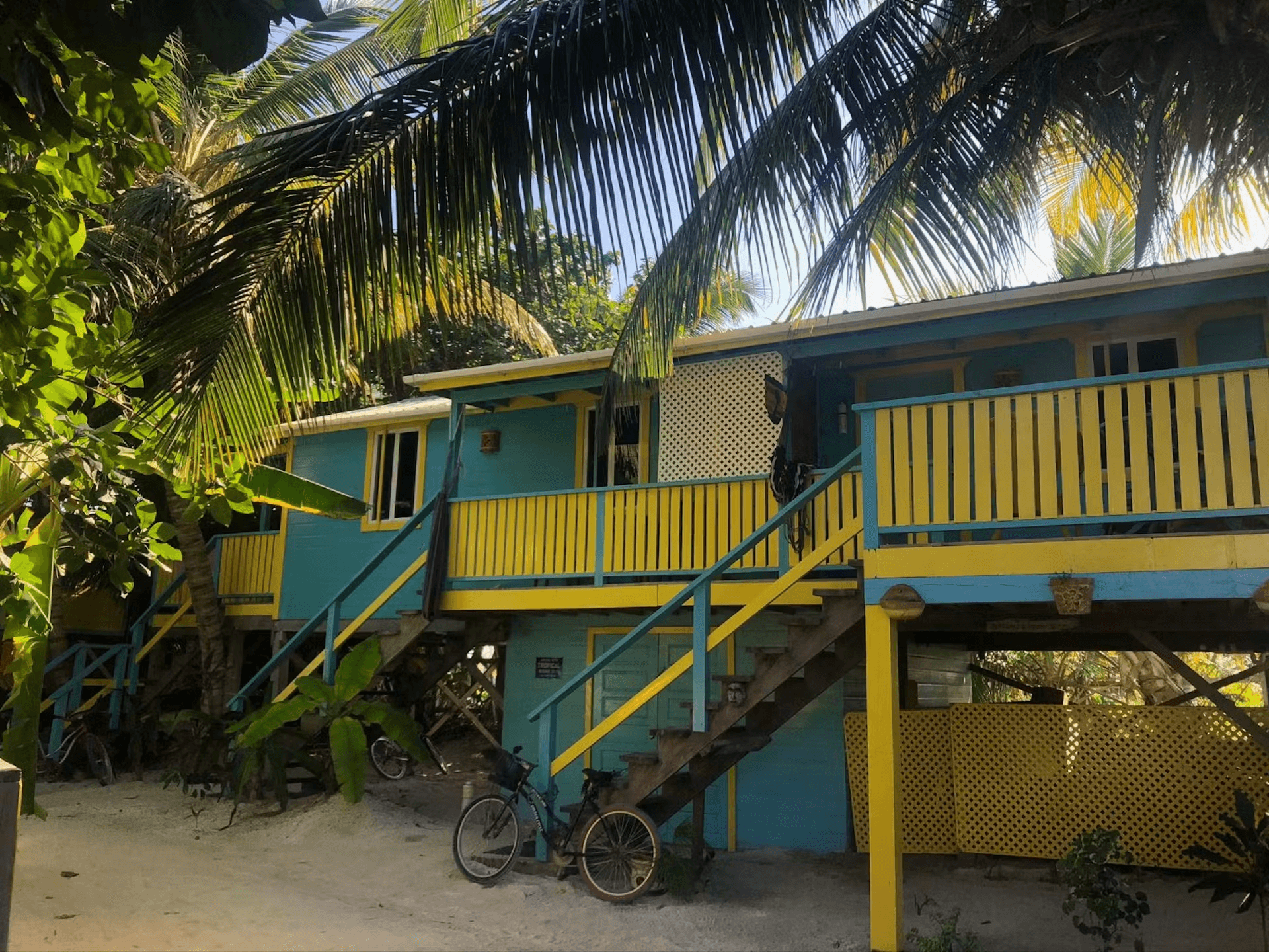 Exterior of a colorful blue and yellow cabana with stairs leading to second level, framed by tropica