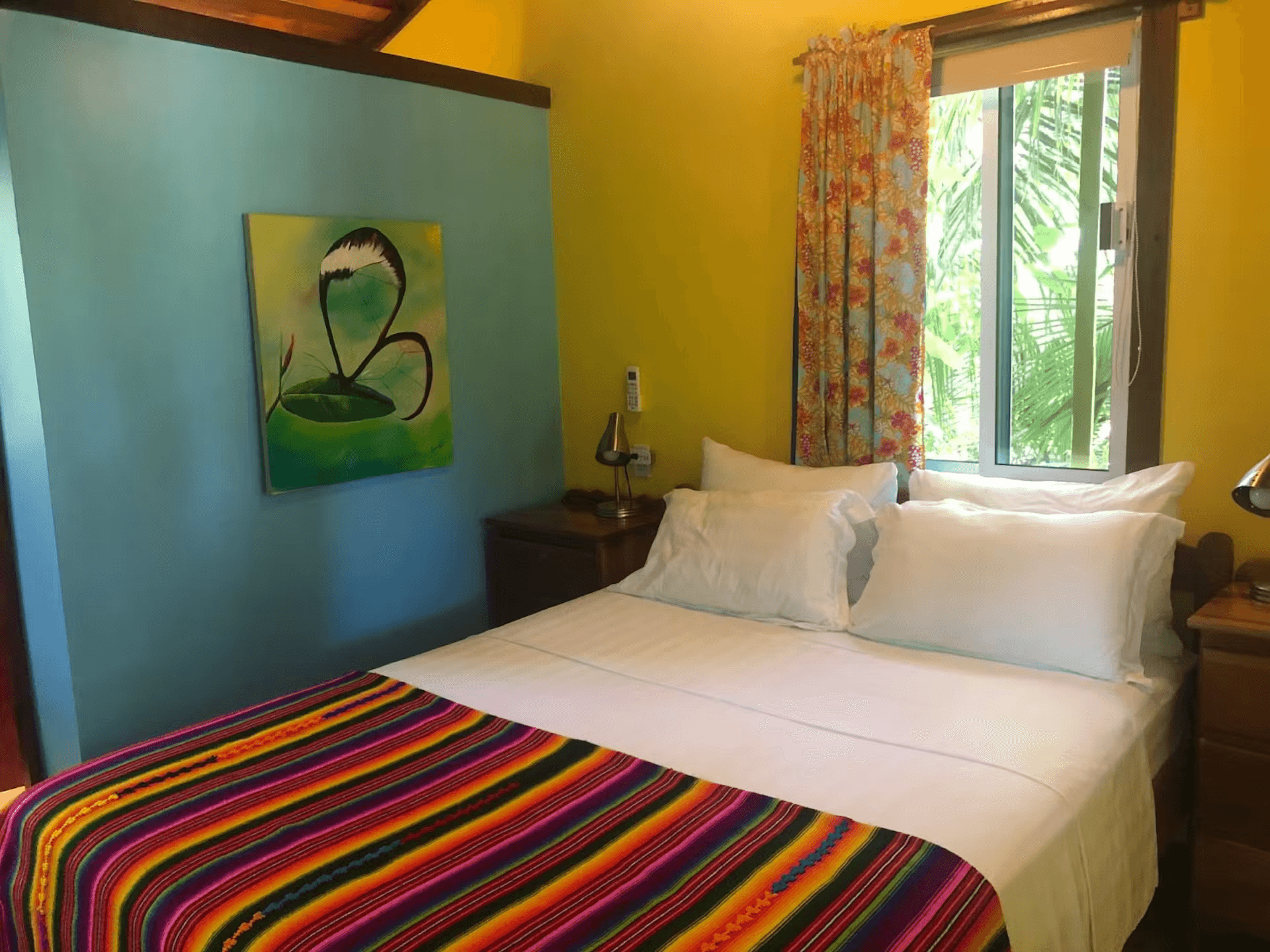 Blue and yellow painted bedroom with queen bed featuring striped bedspread and white sheets and pill