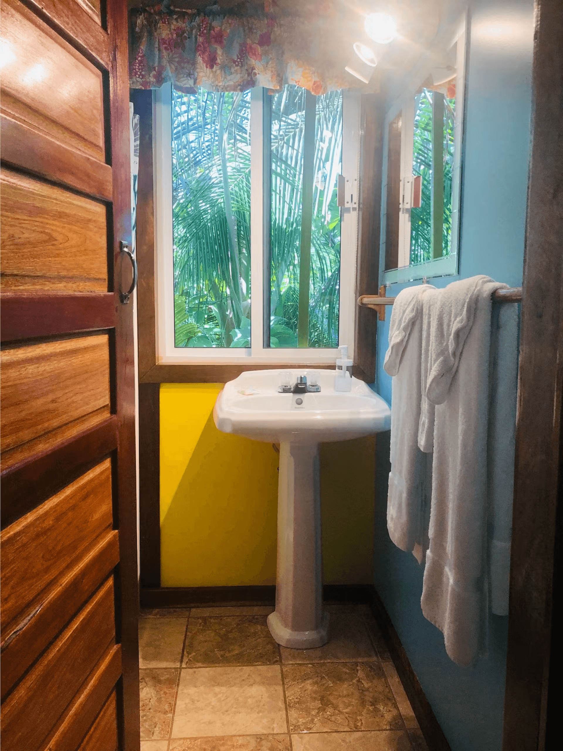 Bathroom with yellow and blue painted walls, white pedestal sink, with window above, and plush white
