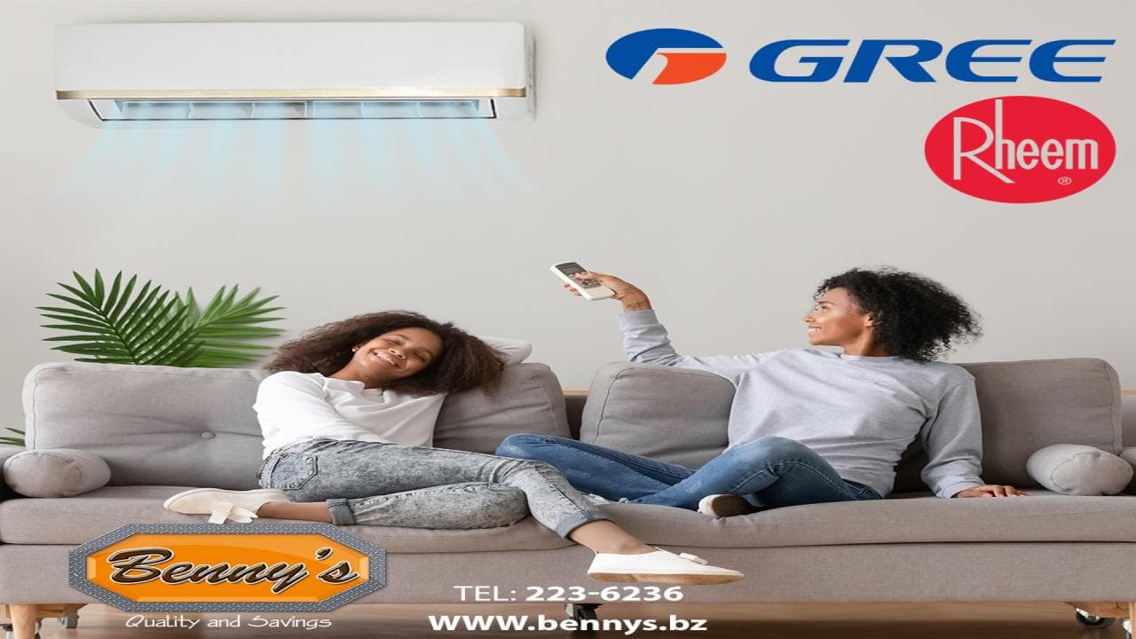 Two women relax on a couch while using a remote control and an air conditioning unit is visible above them.