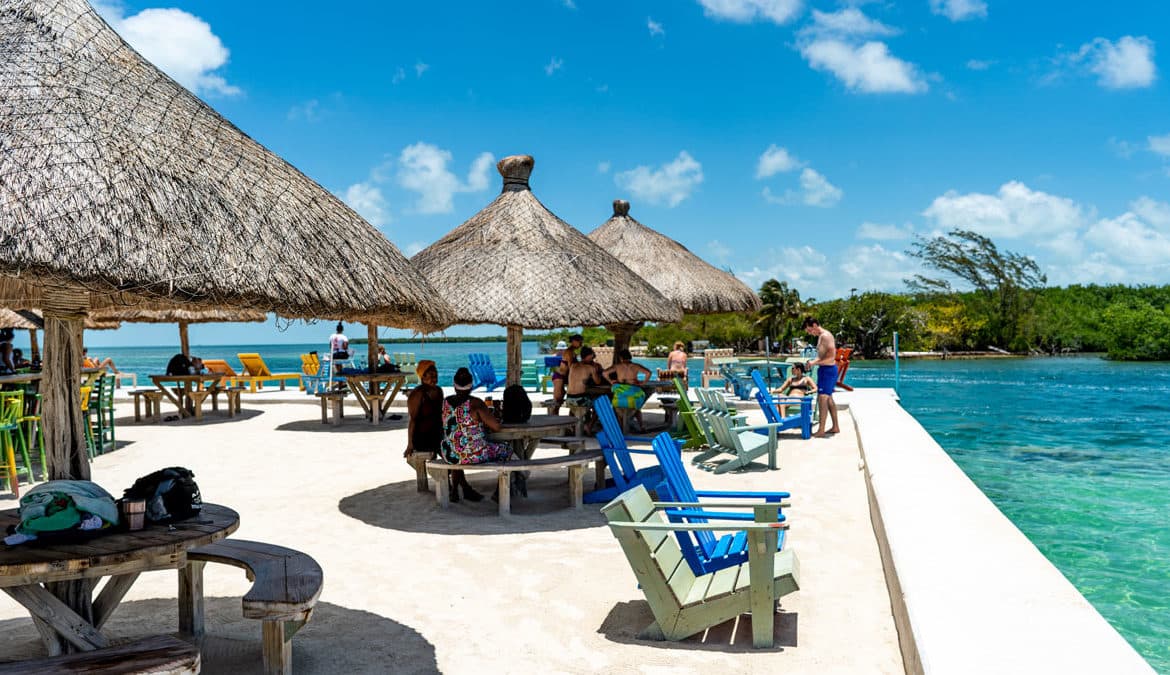 A vibrant beachside scene with thatched umbrellas and colorful chairs, where people gather by the turquoise water. A vibrant beachside scene with thatched umbrellas and colorful chairs, where people gather by the turquoise water.