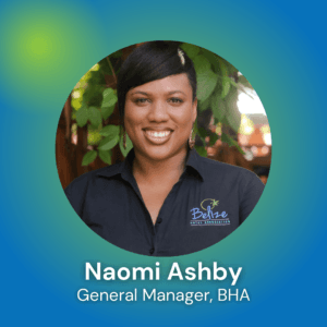 A woman smiling in a black shirt with a logo, framed by greenery, representing Naomi Ashby, General Manager of BHA.