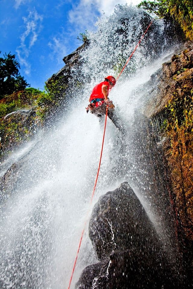 A climber rappels down a waterfall amidst splashing water and a blue sky.