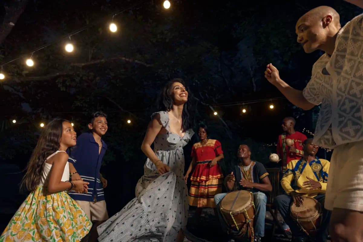 A lively group of children and adults dance joyfully under string lights at an evening celebration.