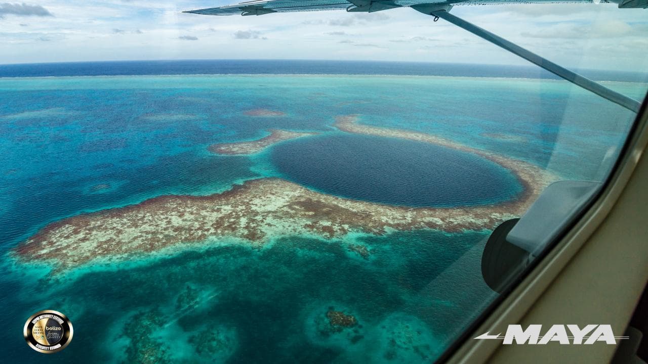 Aerial view of a circular blue hole surrounded by turquoise waters and coral reefs.