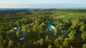 Aerial view of a lush, green landscape with a cluster of buildings surrounded by trees.