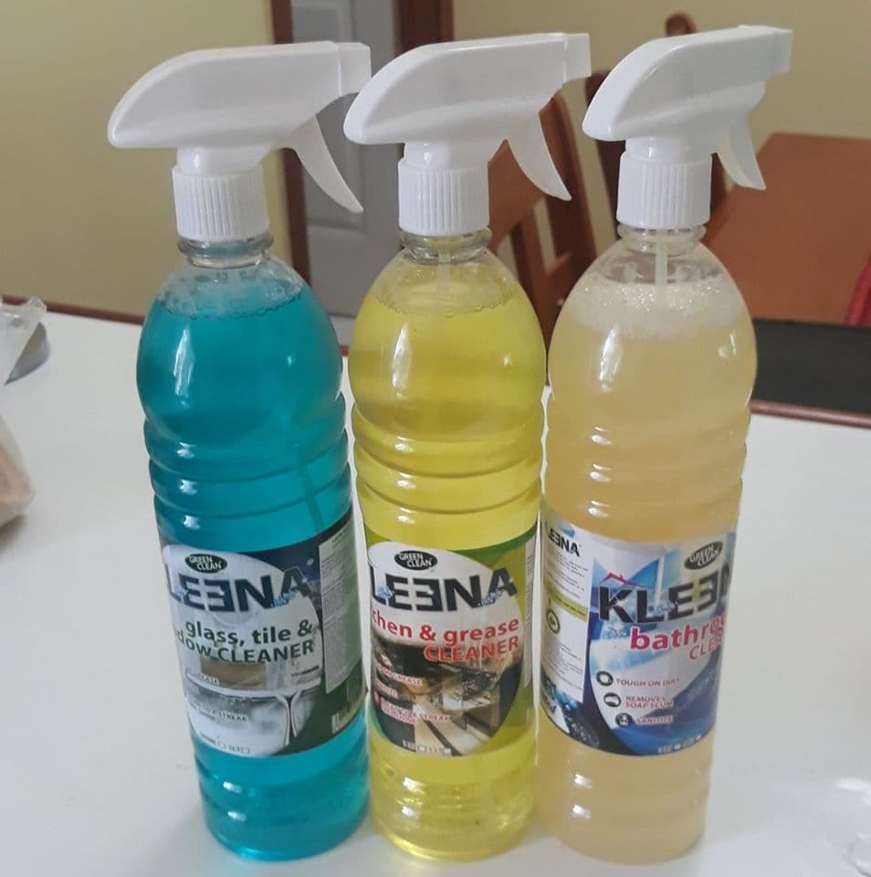 Three cleaning spray bottles-blue for glass, yellow for kitchen grease, and a beige one for bathrooms-are arranged on a countertop.