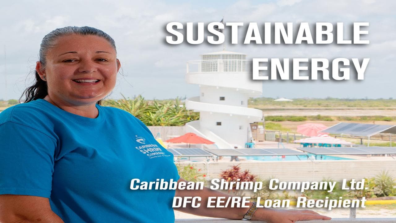 A smiling woman in a blue shirt stands in front of a shrimp company facility, highlighting sustainable energy initiatives.