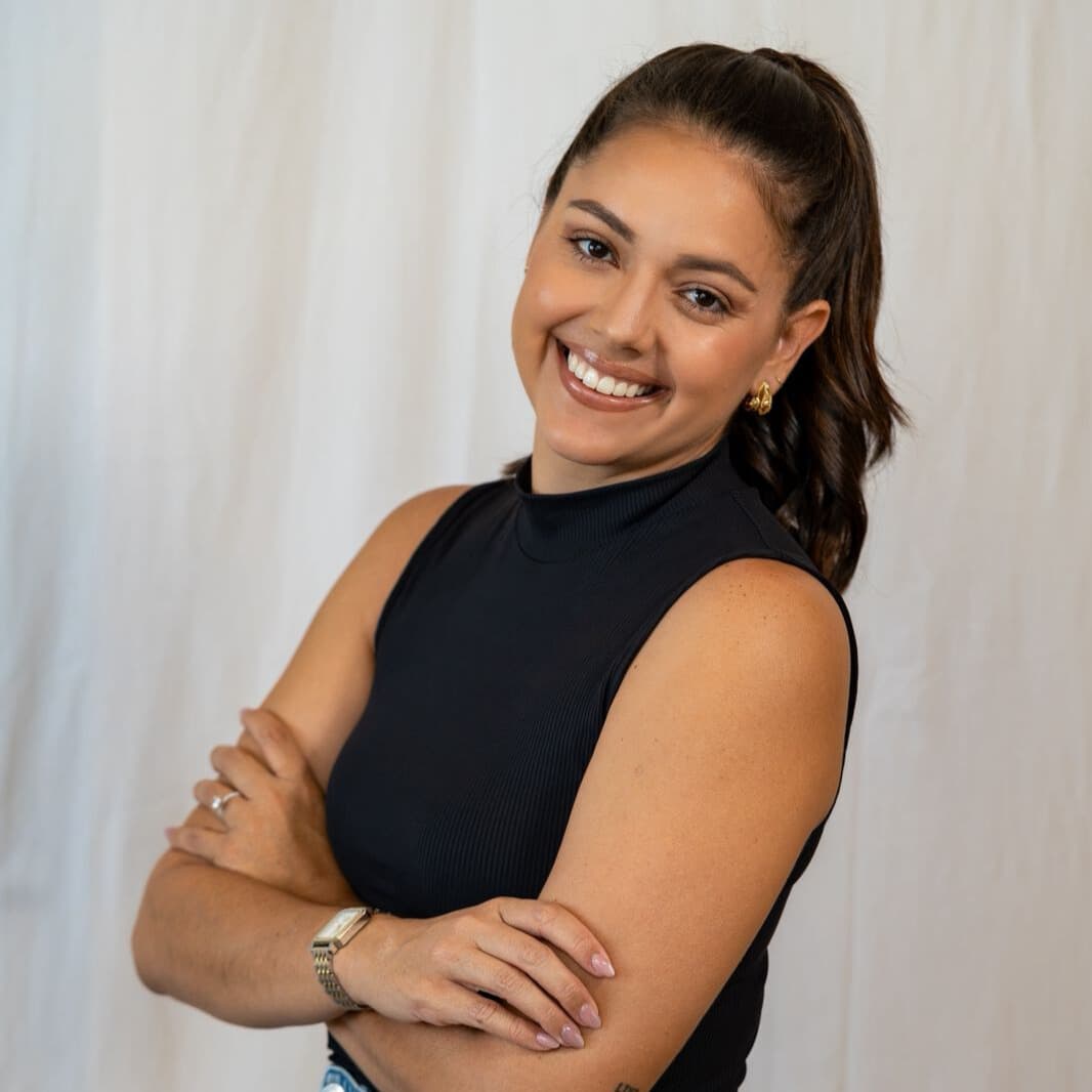 A smiling woman with long brown hair stands with her arms crossed against a light backdrop.