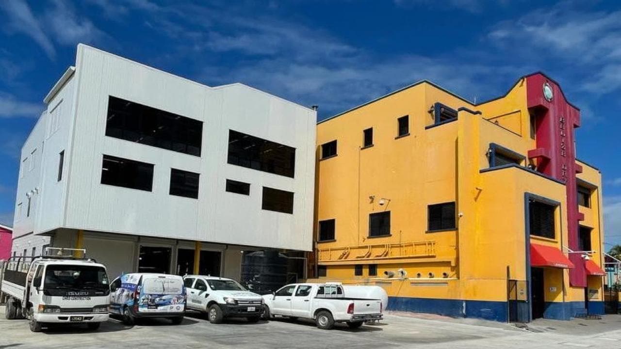 A white and yellow commercial building with multiple vehicles parked in front under a blue sky.
