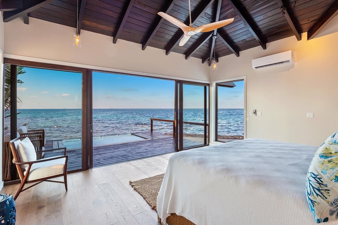 A bright bedroom with a view of the ocean through large glass doors.