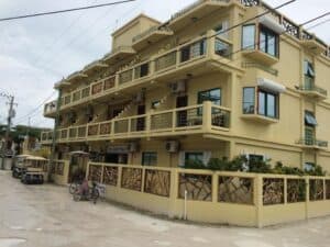 Three-story yellow building with balconies and a decorative fence on a cloudy day.