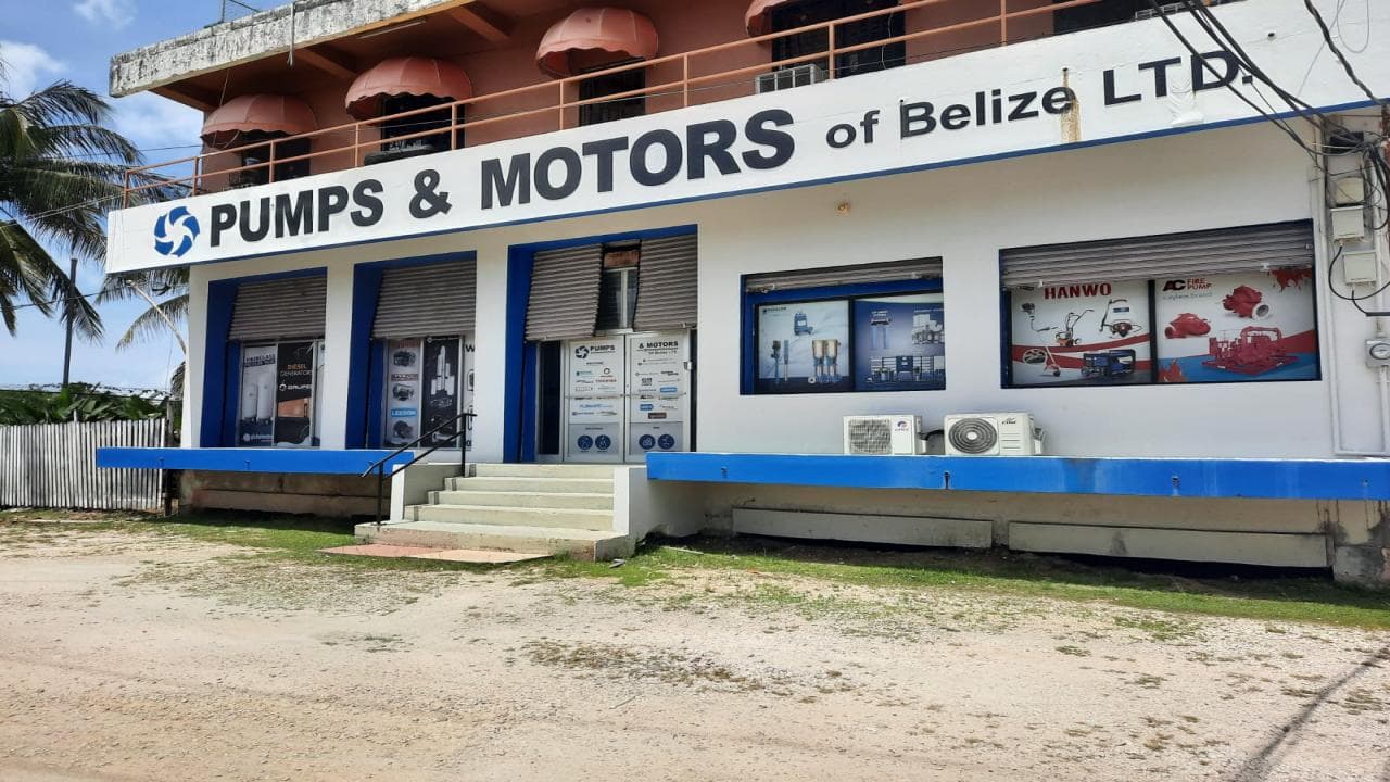 Exterior view of a building labeled "Pumps & Motors of Belize LTD" with windows displaying various products.