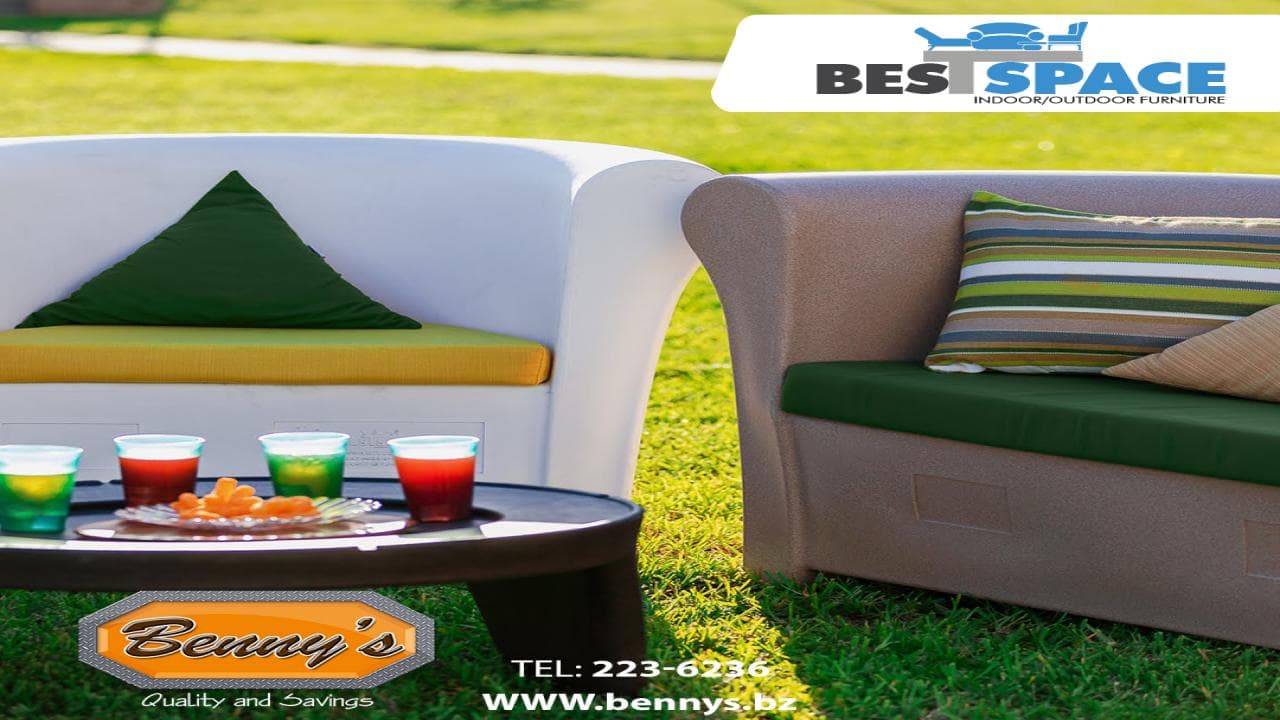 A pair of outdoor lounge chairs with colorful cushions and drinks on a table, set on a grassy area.