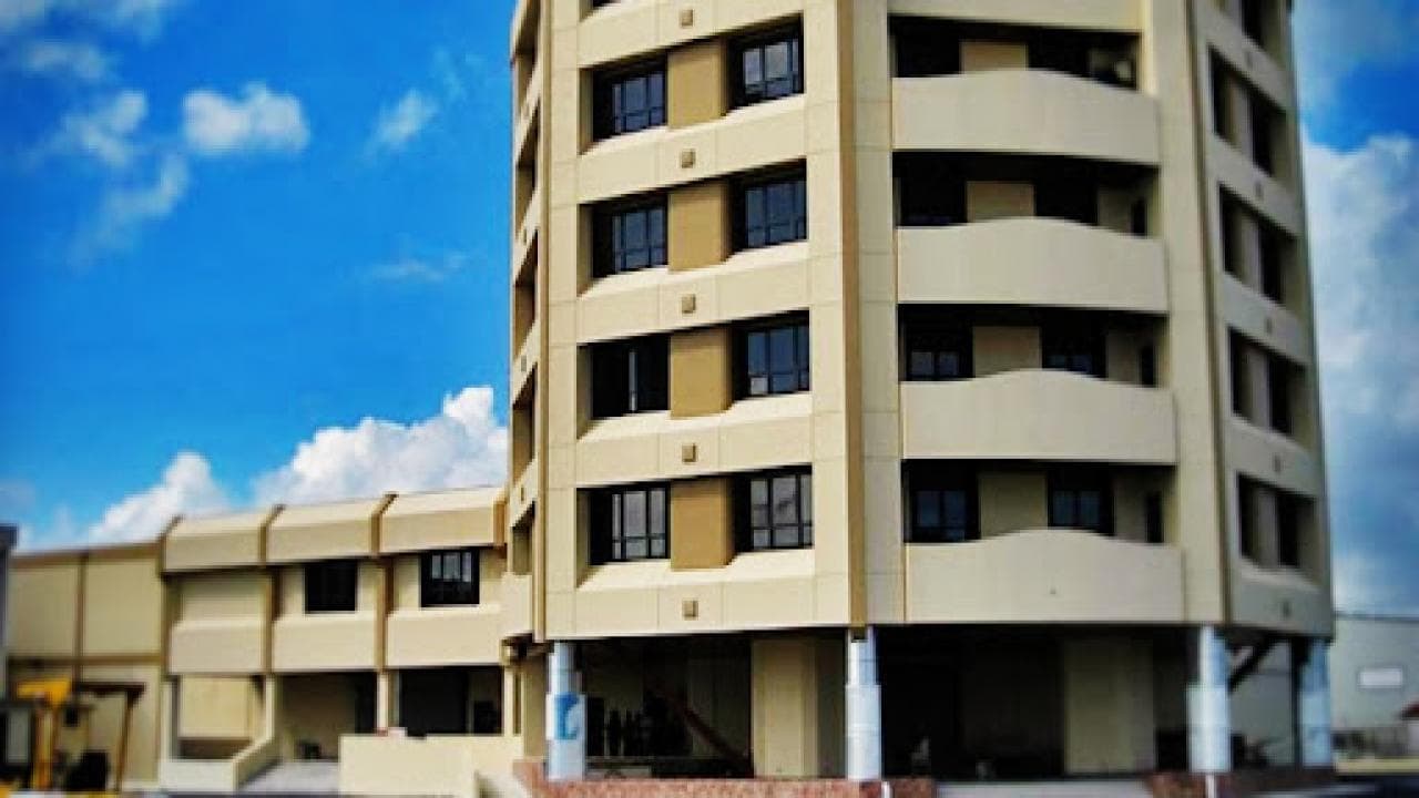 A tall beige building with multiple windows against a blue sky with scattered clouds.