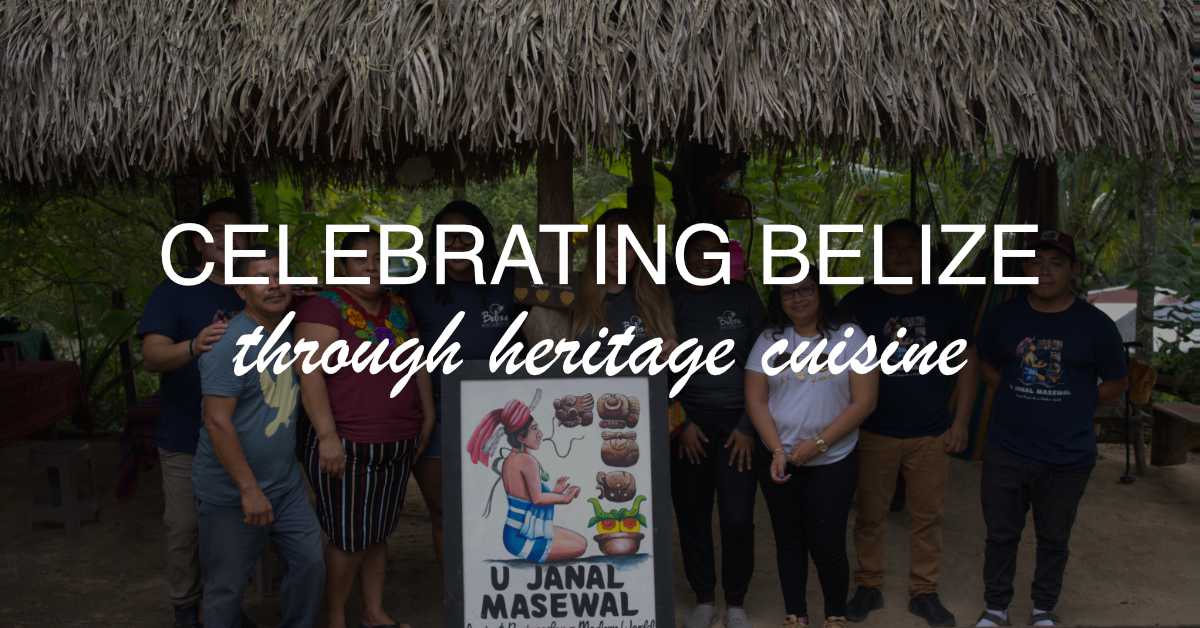 A group of people stands in front of a sign celebrating Belizean heritage cuisine beneath a thatched roof. A group of people stands in front of a sign celebrating Belizean heritage cuisine beneath a thatched roof.