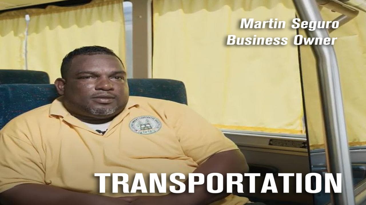 A business owner sits in a bus, with yellow curtains and the word "TRANSPORTATION" prominently displayed.