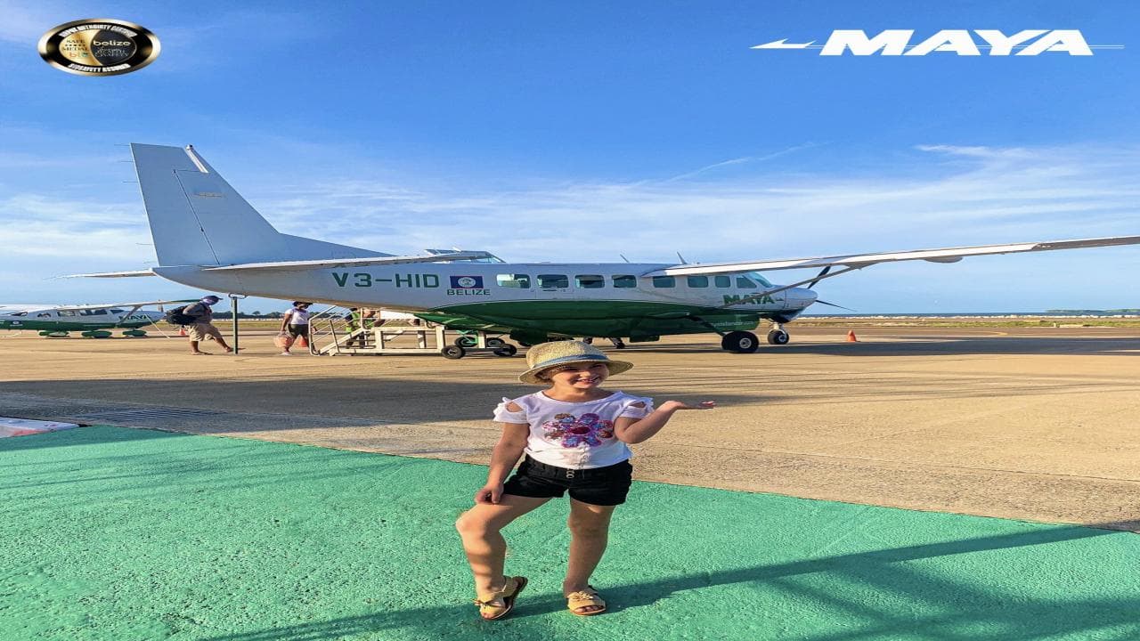 A child poses cheerfully in front of a small airplane on a sunny airport tarmac.