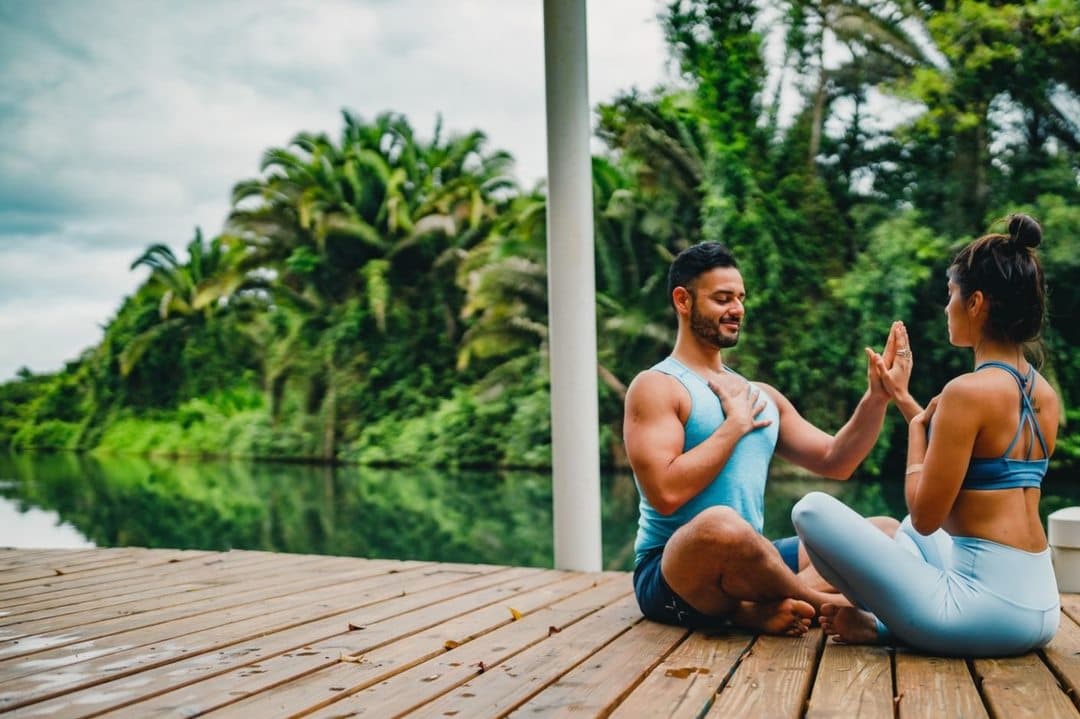 A man and woman practice yoga on a wooden dock beside a serene, lush landscape. A man and woman practice yoga on a wooden dock beside a serene, lush landscape.
